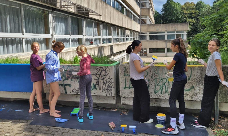 Schülerinnen malen Betonteile des Burgau-Gymnasiums bunt an.