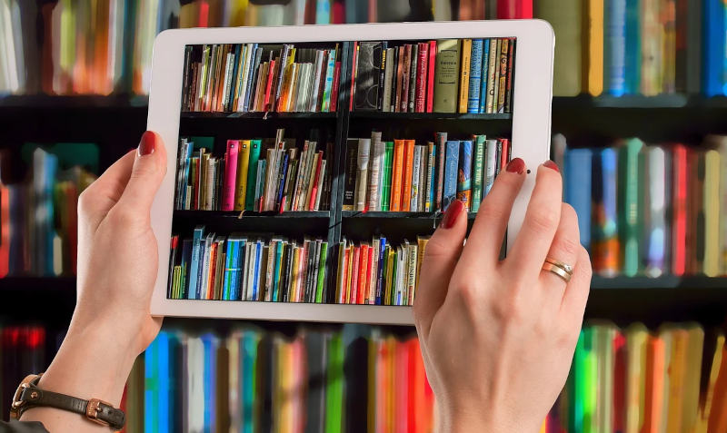 Ein Tablet vor einem Bücherregal, auf dem Display erkennt man das Bücherregal.