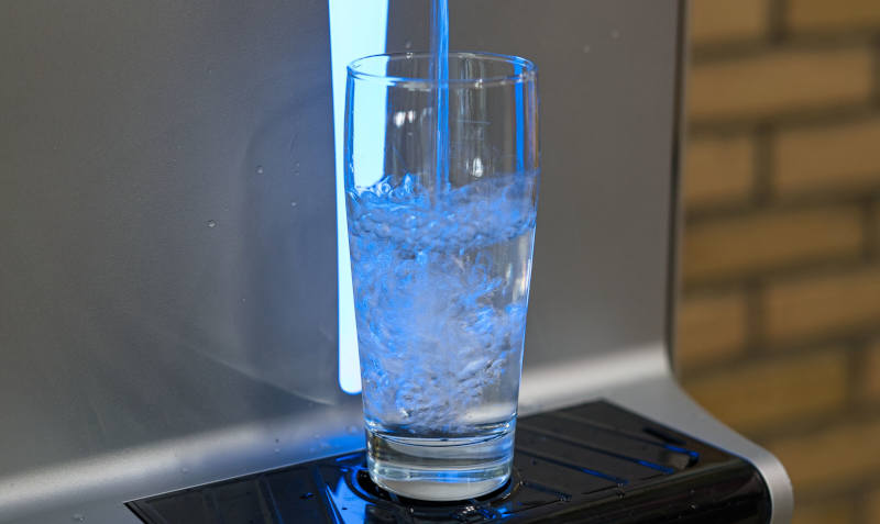 Ein Glas unter einem Wasserspender, es läuft Wasser ein.